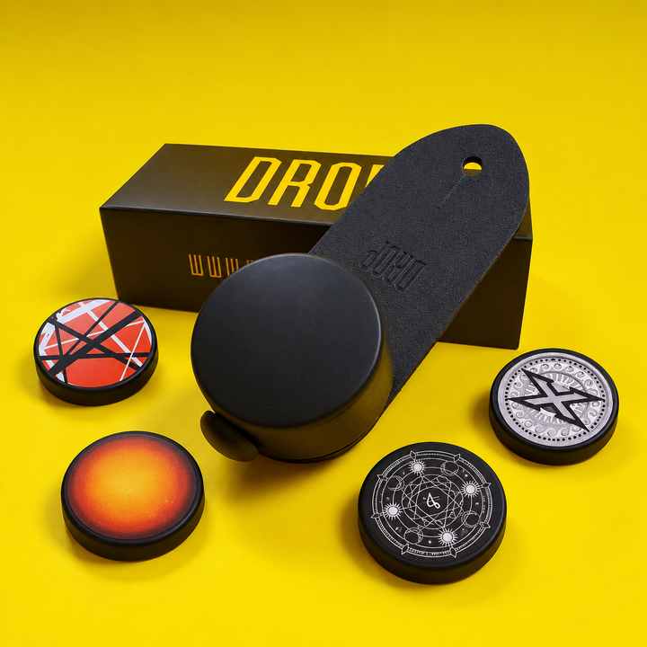 One DROP guitar strap adjuster with package and interchangeable custom logo caps on a yellow background